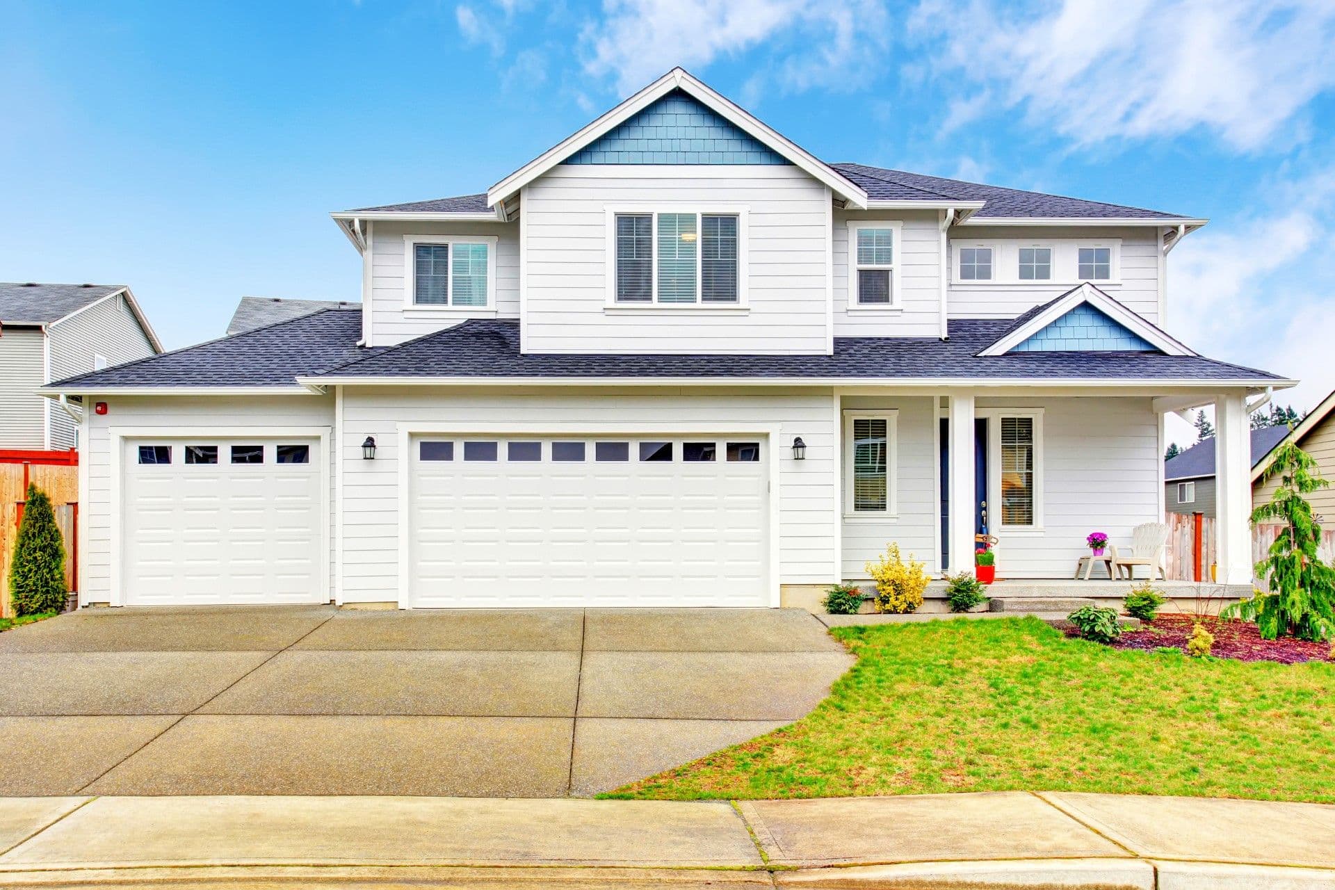 Concrete driveway - White two-story suburban house with two-car garage, front porch, manicured lawn and landscaping under clear blue sky